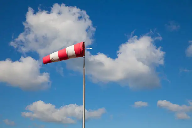 Bright cumulus clouds with striped windsock in clear blue sky at a beach of the Netherlands North Sea region