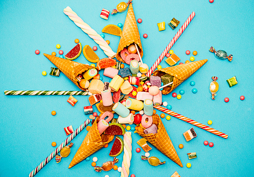 Candy splash out of five sweet cones. Candy mix with jellybeans, marshmellows, cones, gummy candy, hard candies, lollipop, sweets and bonbons on blue background.