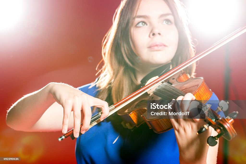 Violin Music Beautiful young woman playing the violin in the spotlight. Shooting in studio on a red background. Focus on violin in foreground 2015 Stock Photo