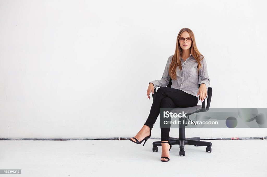 Portrait of beautiful business woman sitting on chair Portrait of young beautiful business woman sitting on chair against white wall. Women Stock Photo