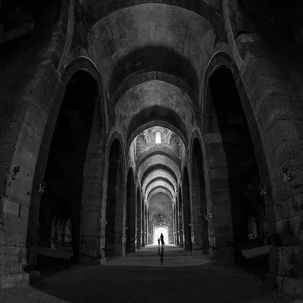 Little boy and his mother walking toward exit at the end of dark tunnel.They are hand in hand.There are big and high columns in both sides of frame.The bright door is in the middle of square frame.Shot with a full frame DSLR camera and a wide angle lens in horizontal composition then cropped to square.