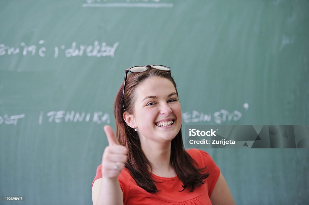 Happy schoolgirl Smiling schoolgirl in front of blackboard showing thumb up Adolescence Stock Photo