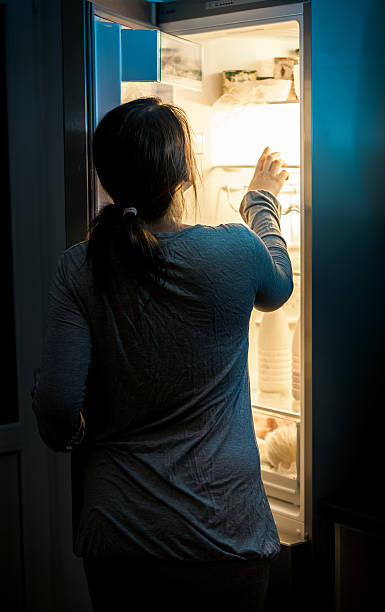 hungry woman looking in fridge at late night Portrait of hungry woman looking in fridge at late night fridge light stock pictures, royalty-free photos & images