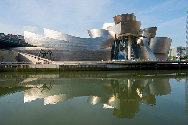 Guggenheim Museum of Bilbao Bilbao, Spain - May 8, 2014: People walking on a promenade beside the Ria Estuary pass by the Guggenheim Museum, designed by Frank Gehry, in Bilbao, Spain. frank gehry building stock pictures, royalty-free photos & images