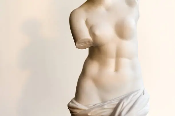 Close-up of a vintage copy statue of Venus (or Aphrodite) de Milo - a famous Greek sculpture dating back to about 100 BC and found in 1820 on the Aegean island of Milos - in a ray of evening sunlight. The copy statue is made of unglazed, white porcelain, also known as bisque, or Parian.