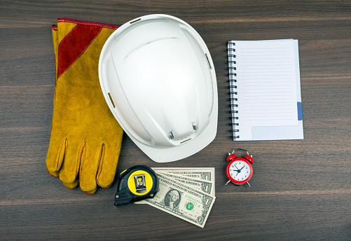 Construction gloves with helmet and alarm clock on wooden table