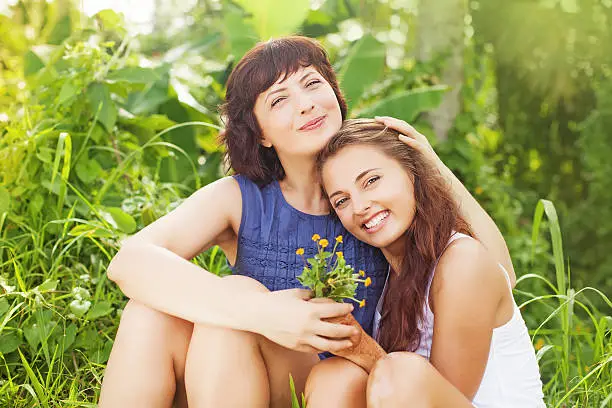 caucasian mother and daughter sitting and hugging each other in a summer field (looking at camera)