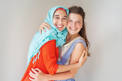 friendship of the religions concept: muslim and christian girl  standing together leaning and smiling at camera