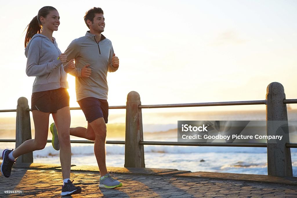 Sticking to their exercise routine while on vacation A young couple jogging on the promenade at sunset Couple - Relationship Stock Photo