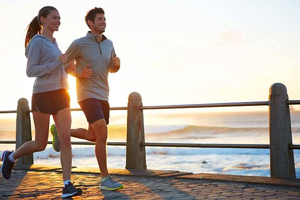 Sticking to their exercise routine while on vacation A young couple jogging on the promenade at sunset female jogger sunset stock pictures, royalty-free photos & images