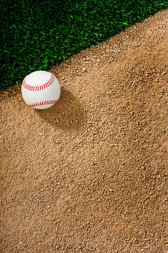 Looking down on a Baseball in the dirt next to grass.