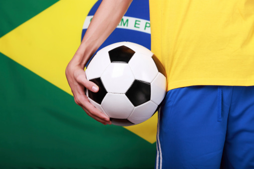 Holding a soccer ball next to Brazil flag 