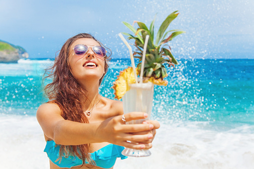 happy tourist woman stretching a tropical cocktail on a beach