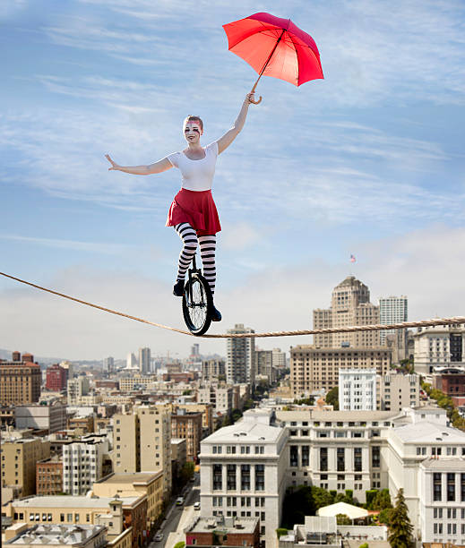Circus Tightrope Walker on a Unicycle Composite photo of a attractive feamle circus performer using a tightrope while riding  a unicycle over a big city. tightrope stock pictures, royalty-free photos & images