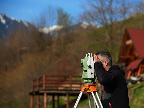 side view of land surveyor measuring and capculating, looking through total station.
