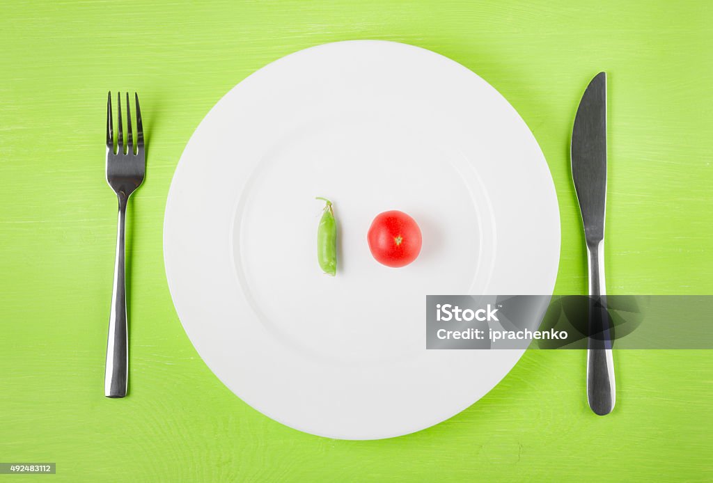 concept of dietary restrictions the concept of dietary restrictions, healthy lifestyle, diet,  weight loss, anti-obesity, healthy diet. Small tomato, green peas, on a plate, knife, fork on the table, top view 2015 Stock Photo