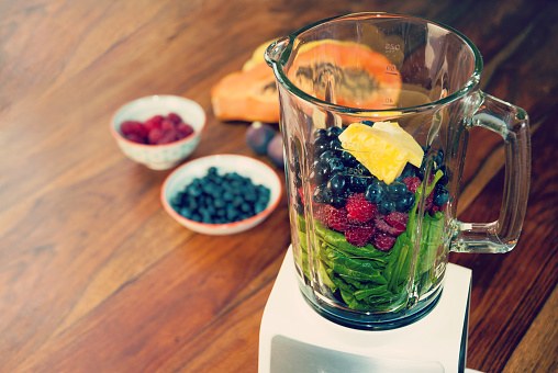 Fruits and vegetables as ingredients for a healthy smoothie: papaya, figs, lemon, blueberries, pomegranate seeds, raspberries, pineapple and baby spinach