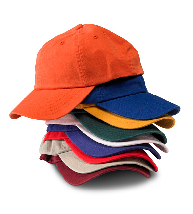 A stack of multicolored baseball caps on a white background with an orange cap on top. There is a clipping path which may be used to delete the shadow if desired.