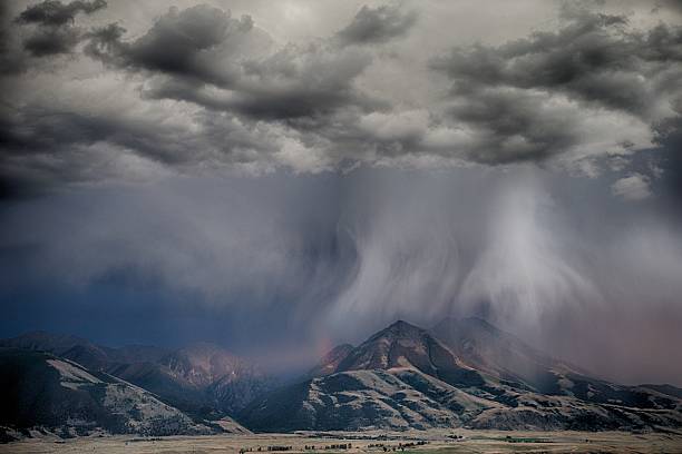 A summer Thunderstorm moves across Paradise Valley, Montana and the Absaroka Mountain Range as a beam of sunlight cuts through the darkness, creating a small rainbow near Emigrant Peak.