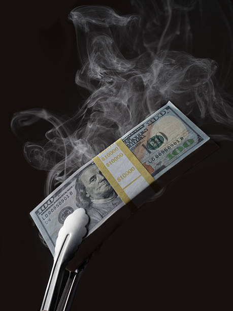 Smoking stack of $100 dollar bills held in barbecue tongs. stock photo