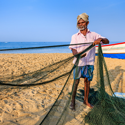 Indian fisherman at work. Fisherman are checking and repairing fishing net, early morning, Kerala, India.