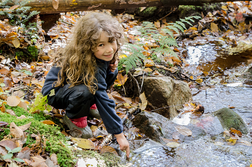 Little girl touching cold water of small river while looking at camera during a nice day af autumn. This is at Le