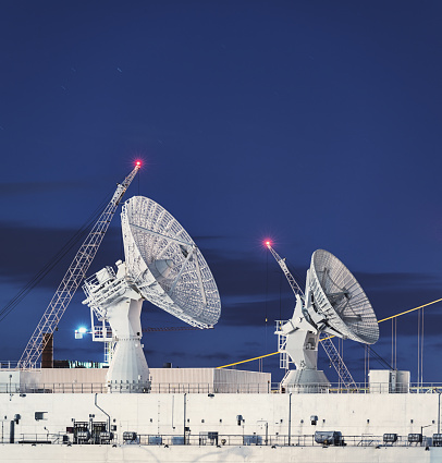 Satellite dishes perched high atop the deck of a vessel used in tracking rocket trajectories. Long exposure.