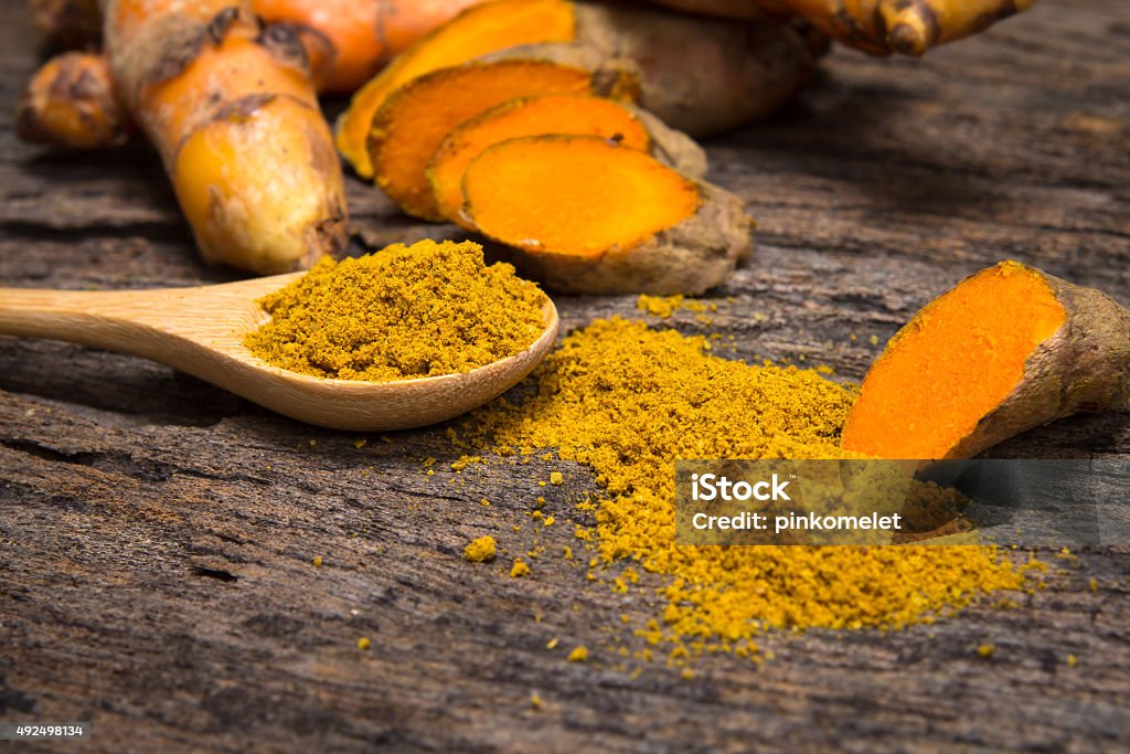 turmeric powder in spoon and roots on wooden plate the turmeric powder in spoon and roots on wooden plate Turmeric Stock Photo