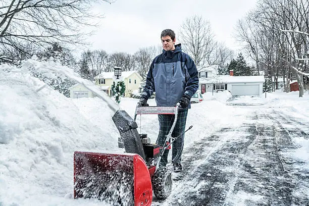 A young man is using a snowblower on a slushy, slippery winter snow suburban home driveway. Western New York State, USA in early January.