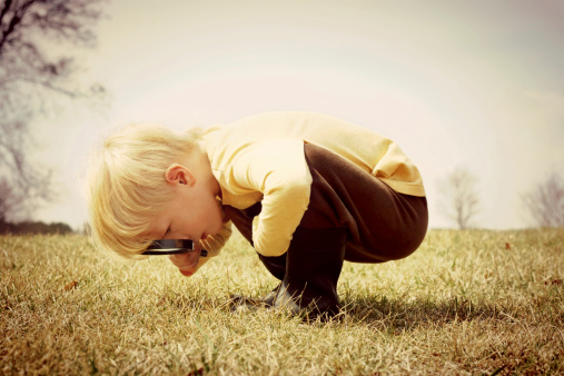 A young child is bending down looking in the grass, investigating something with a magnifying glass.  Vintage style color.
