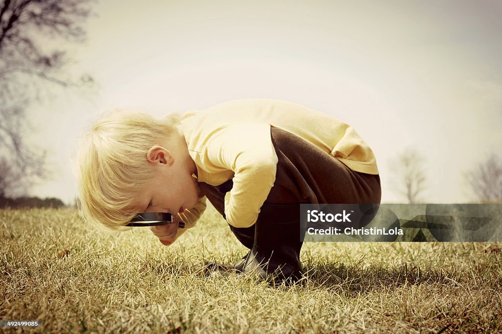 Young Child looking through Magnifying Glass A young child is bending down looking in the grass, investigating something with a magnifying glass.  Vintage style color. Curiosity Stock Photo