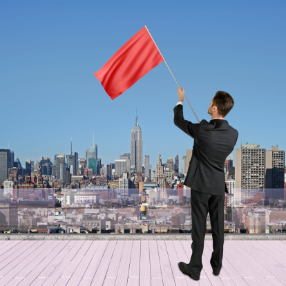 businessman standing on roof with red flag