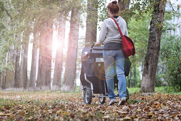 istock Mom with stroller walks in autumn park alley 492520532