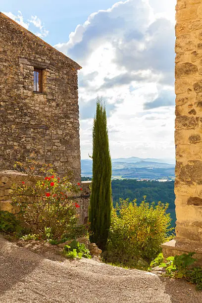Fabulous view from the well restored 612m high situated medieval provencial village, overlooking the Durance valley. Cypress tree and red roses in front.