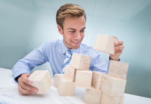 Happy young business man building a project with wooden cubes at the office