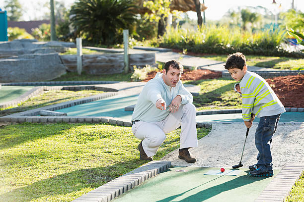 Father (30s) and son (5 years) playing miniature golf.