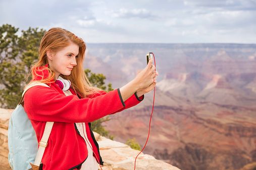 A teenage girl takes a selfie of herself at the Grand Canyon National Park in Arizona -- or alternatively, a teenage girl takes a photo of the Grand Canyon.