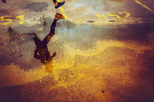Young person running over the parking lot. High angle view of a runner's legs and its reflection in the water.