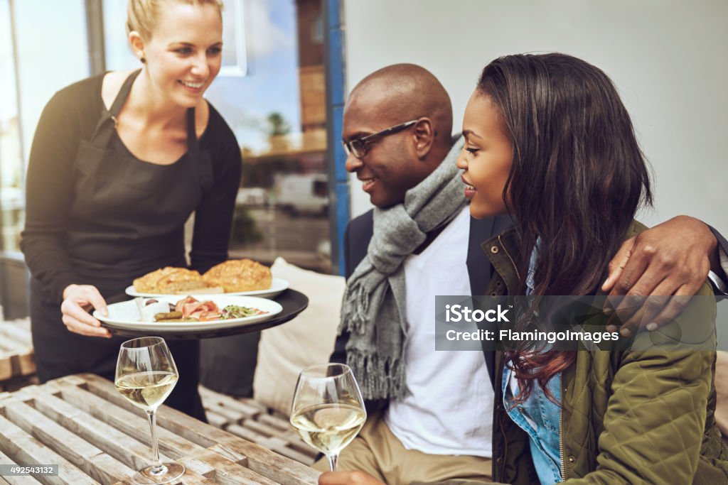 Waitress serving food to an African couple Waitress serving food to an affectionate African American couple sitting arm in arm at a restaurant table Serving Food and Drinks Stock Photo