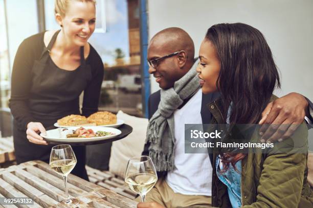 Waitress Serving Food To An African Couple Stock Photo - Download Image Now - Serving Food and Drinks, Couple - Relationship, Service