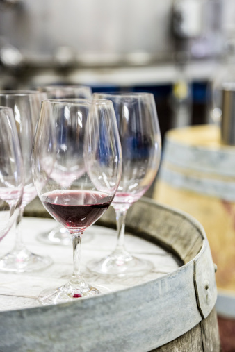 A wine glass partly filled with red wine rests among employ glasses on a wine barrel in a tasting room.
