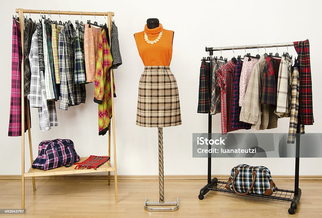 Colorful wardrobe with tartan clothes and accessories. Dressing closet with plaid clothes arranged on hangers and an outfit on a mannequin. Dressmaker's Model Stock Photo