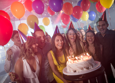 Woman with friends celebrating on her birthday party and about to blow the candles on the cake