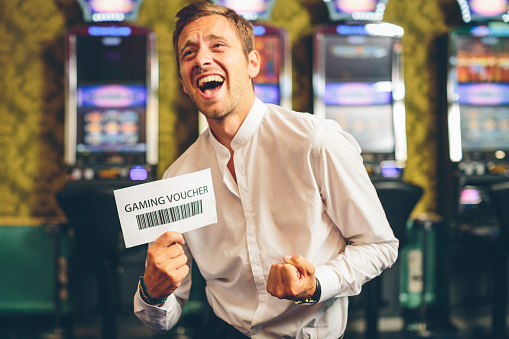 Happy Man Showing a Gaming Voucher. Slot Machine on the background. Some motion blur in image. +++ for the inspector, the voucher is a fake +++