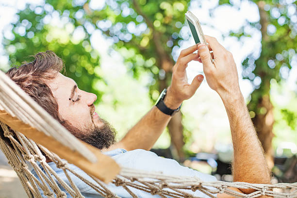 istock caucasian man lying in hammock with mobile phone 492550060