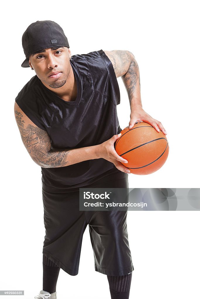 Studio portrait of basketball player wearing white cap. Studio portrait of basketball player wearing black cap standing and holding ball isolated on white. Active Lifestyle Stock Photo