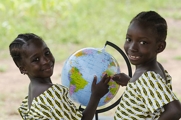 Two Beautiful African Children Pointing to Africa on Globe Young African black girls playing with a globe pointing to Africa with a light smile. Educational symbol for African children. poverty child ethnic indigenous culture stock pictures, royalty-free photos & images