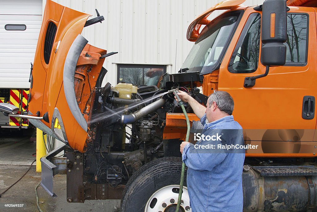 Mechanic washes truck before servicing Shows mechanic with hose washing engine compartment under hood, hood raised. Also shows truck mount plow frame. Diesel Fuel Stock Photo