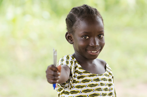 Education symbol: little African black teenage girl holding pen in the air lightly smiling to the camera. African children need education since it is the most important thing for a better future.