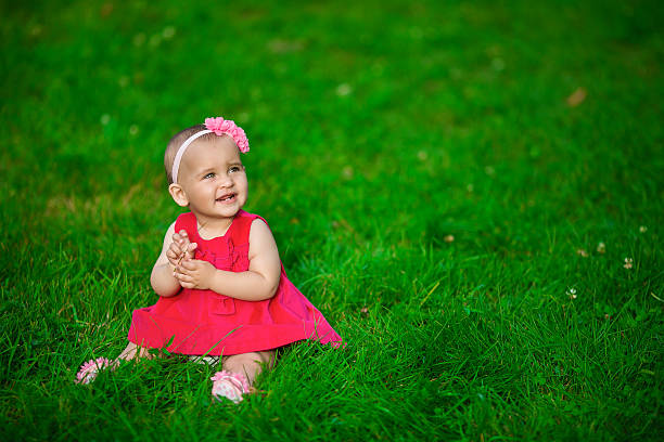 istock Baby in a red dress sits on a grass 492570916